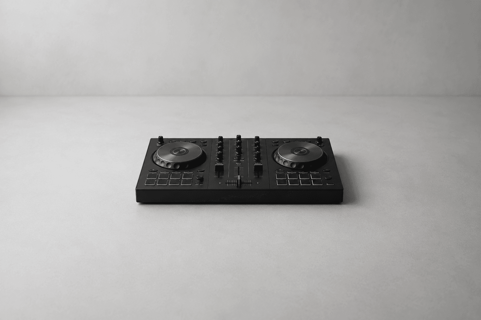 A matte black two-deck DJ controller with two circular metal jog wheels, two banks of rubber performance pads, channel faders and a crossfader, photographed from a raised angle on a plain pale grey surface with wide empty space on every side