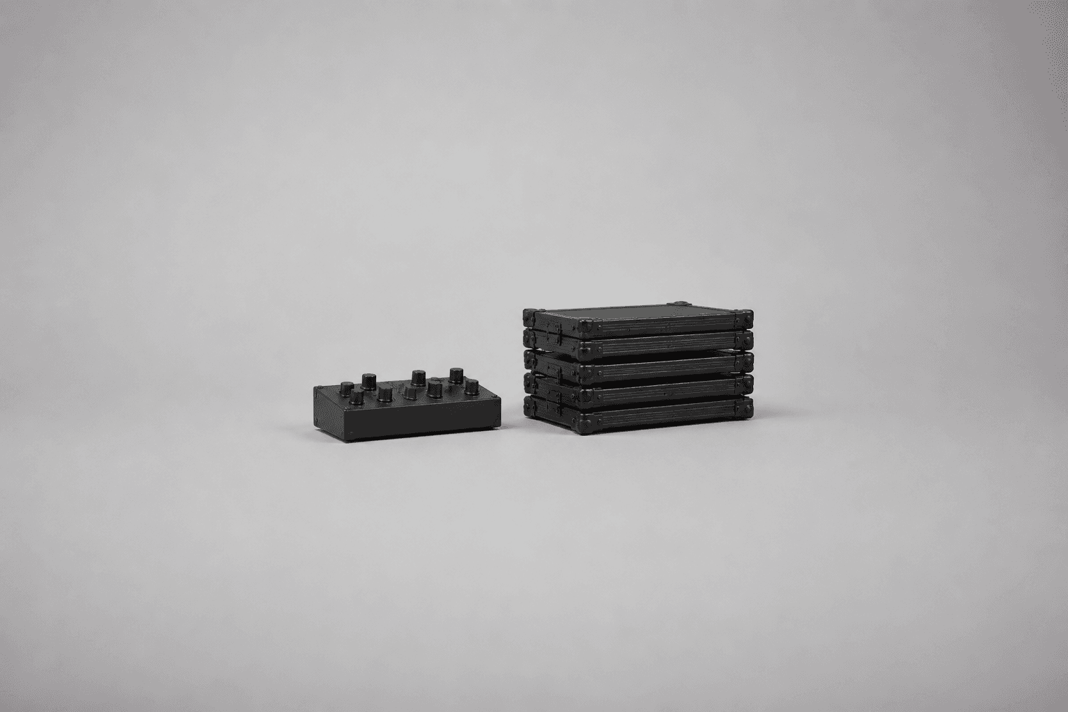 A single small matte black synthesiser box with a handful of unlabelled knobs sitting on the left, and a stack of five identical plain black flight cases sitting on the right, both small and centred in a wide expanse of empty pale grey studio floor