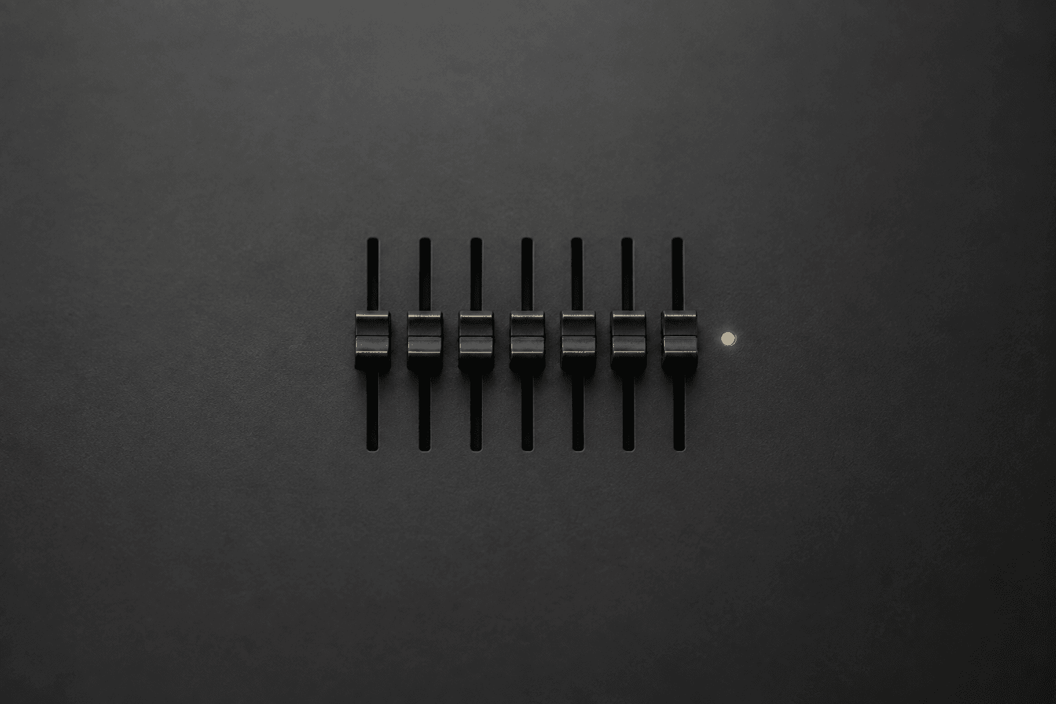 Seven unmarked black mixing-desk faders set to exactly the same height in a level row, with one small amber light beside them, centred on a wide plain charcoal panel